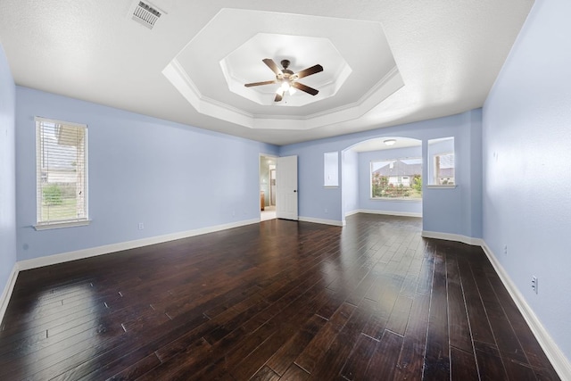110 Starlight Trl, Georgetown, TX 78633 - unfurnished living room featuring a ceiling fan, a tray ceiling, dark wood-style flooring, arched walkways, and baseboards