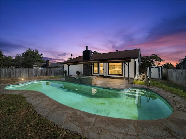 3912 Hillside Dr, Round Rock, TX 78681 - back of house at dusk with a fenced backyard, a patio, a shed, a chimney, and a pool with connected hot tub