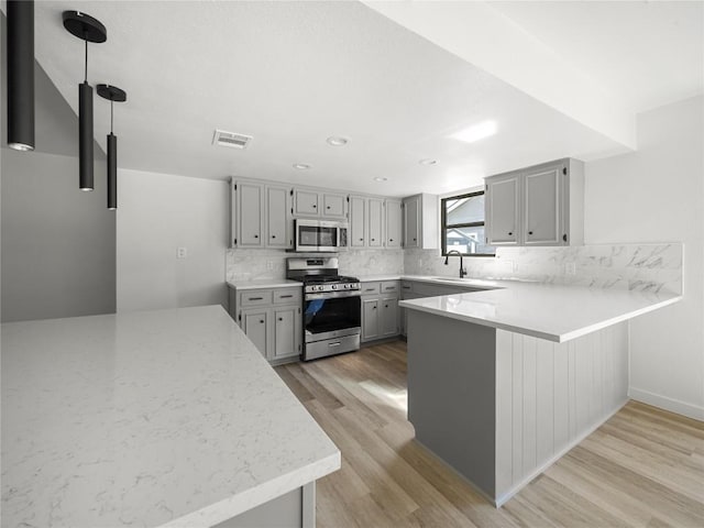 3912 Hillside Dr, Round Rock, TX 78681 - kitchen with appliances with stainless steel finishes, gray cabinetry, light wood finished floors, backsplash, and a peninsula