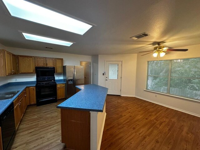 8429 Steamline Cir, Austin, TX 78745 - kitchen with black appliances, dark wood-style floors, a center island, and brown cabinetry