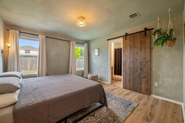 626 Goldenrod St, Kyle, TX 78640 - bedroom with light wood-style floors, baseboards, a barn door, and connected bathroom
