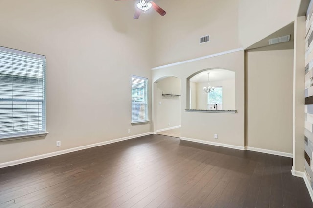 8521 White Ibis Dr, Austin, TX 78729 - unfurnished living room with a chandelier, a ceiling fan, arched walkways, dark wood-style flooring, and a high ceiling