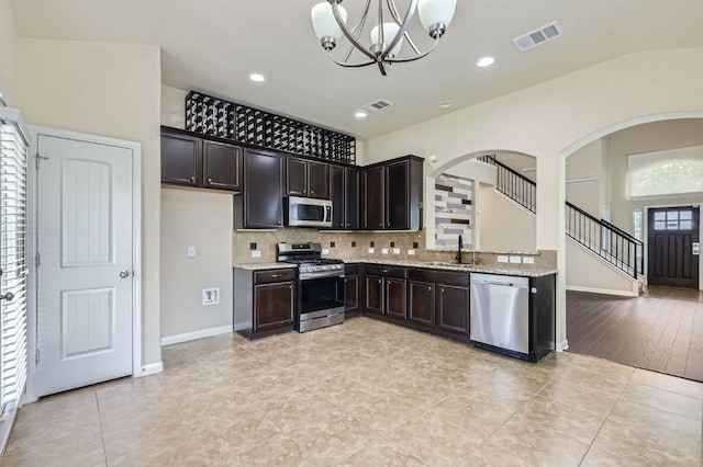 8521 White Ibis Dr, Austin, TX 78729 - kitchen with stainless steel appliances, a chandelier, decorative backsplash, arched walkways, and light stone countertops