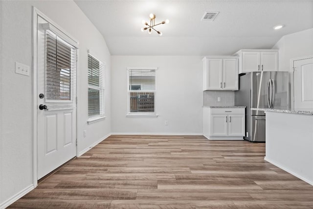 229 Reagor Dr, Taylor, TX 76574 - kitchen with freestanding refrigerator, vaulted ceiling, light wood-style floors, white cabinets, and light stone countertops