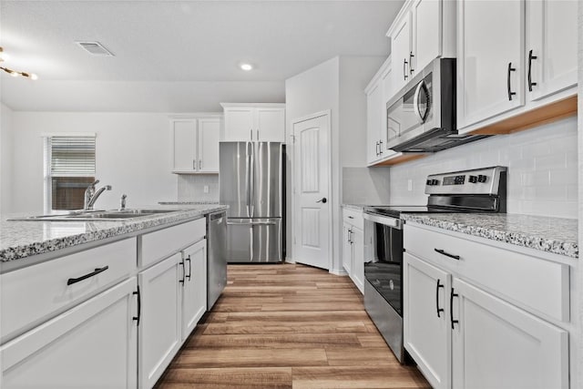 229 Reagor Dr, Taylor, TX 76574 - kitchen featuring appliances with stainless steel finishes, a sink, white cabinets, light wood-type flooring, and recessed lighting