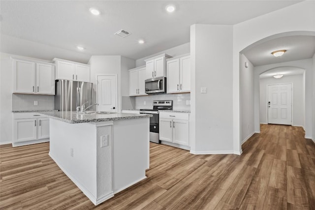 229 Reagor Dr, Taylor, TX 76574 - kitchen with stainless steel appliances, a sink, decorative backsplash, light wood-style floors, and white cabinetry