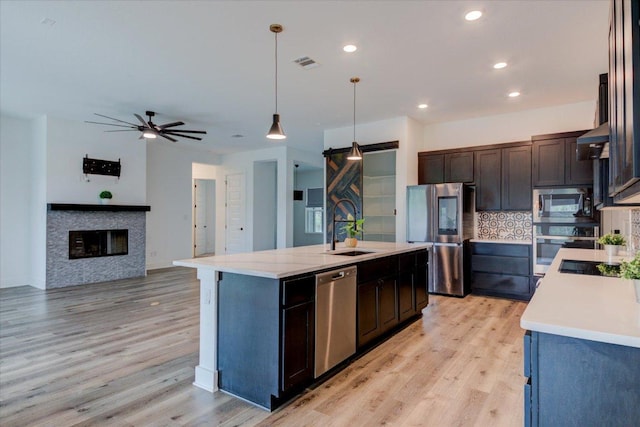 13401 Trail Driver, Austin, TX 78737 - kitchen featuring appliances with stainless steel finishes, a sink, light wood-style floors, decorative backsplash, and a kitchen island with sink