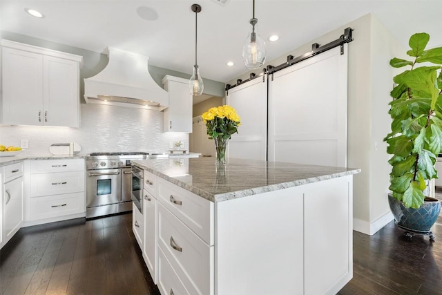 19407 White Horse Cv, Spicewood, TX 78669 - kitchen with custom exhaust hood, double oven range, a barn door, dark wood-type flooring, and a kitchen island