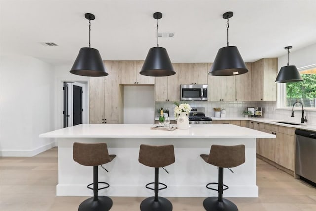 2322 Westoak Dr, Austin, TX 78704 - kitchen with stainless steel appliances, light brown cabinets, light wood-type flooring, backsplash, and a kitchen breakfast bar