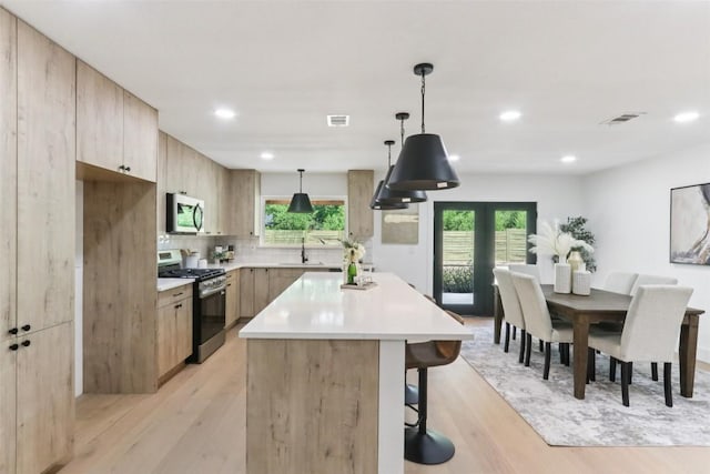 2322 Westoak Dr, Austin, TX 78704 - kitchen featuring stainless steel appliances, a kitchen island, a breakfast bar, light brown cabinetry, and light wood-type flooring
