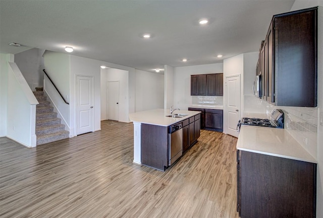 102 George Kimble Cv, Bastrop, TX 78602 - kitchen with appliances with stainless steel finishes, a sink, light wood-style floors, an island with sink, and dark brown cabinetry