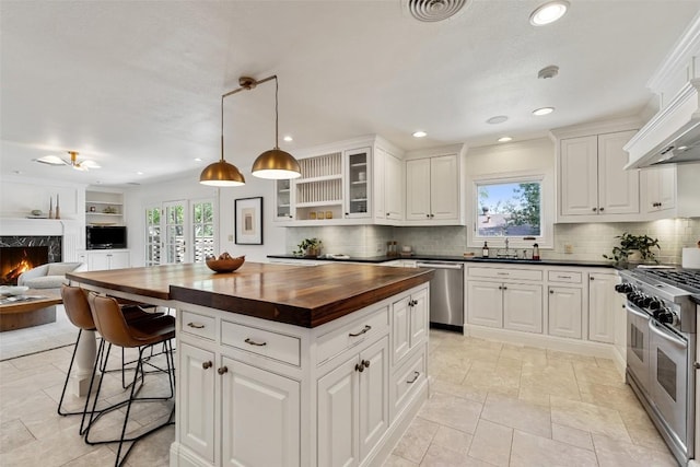 4607 Balcones Dr, Austin, TX 78731 - kitchen with wood counters, stainless steel appliances, open floor plan, a fireplace, and glass insert cabinets