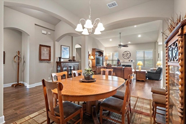 21912 Rock Wren Rd, Spicewood, TX 78669 - dining room featuring ceiling fan, dark wood-type flooring, a chandelier, arched walkways, and a fireplace