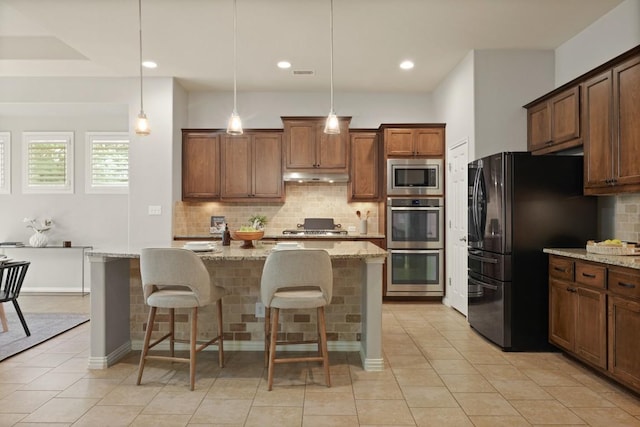 495 Catalina Ln, Austin, TX 78737 - kitchen featuring appliances with stainless steel finishes, under cabinet range hood, tasteful backsplash, a kitchen bar, and light stone countertops