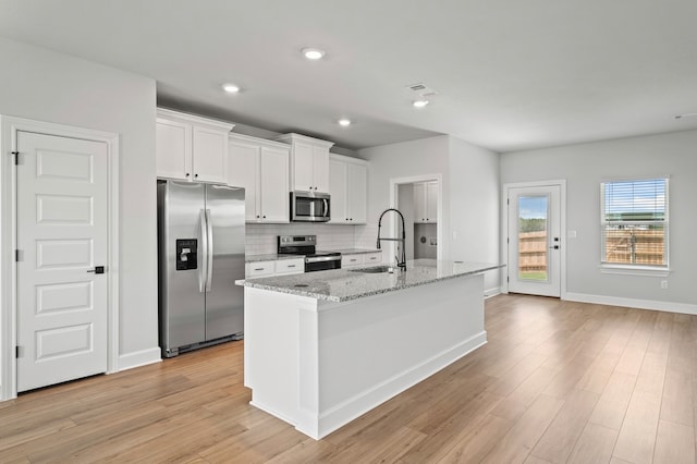 9312 Gladsome Path, Manor, TX 78653 - kitchen featuring appliances with stainless steel finishes, a sink, white cabinets, light wood-style floors, and tasteful backsplash
