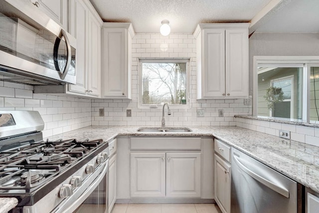 7105 Creighton Ln, Austin, TX 78723 - kitchen featuring appliances with stainless steel finishes, white cabinetry, decorative backsplash, light stone counters, and a textured ceiling
