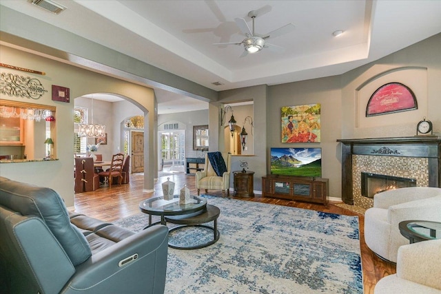 12505 Stapp Ct, Austin, TX 78732 - living room featuring arched walkways, ceiling fan, wood finished floors, a tiled fireplace, and a chandelier