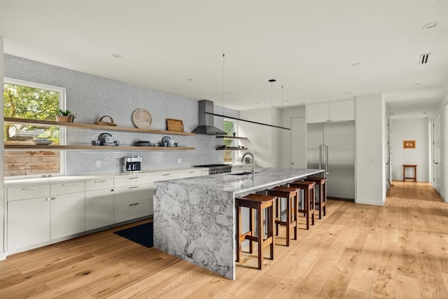 4005 Knollwood Dr, Austin, TX 78731 - kitchen with built in refrigerator, wall chimney exhaust hood, open shelves, a kitchen island with sink, and white cabinets