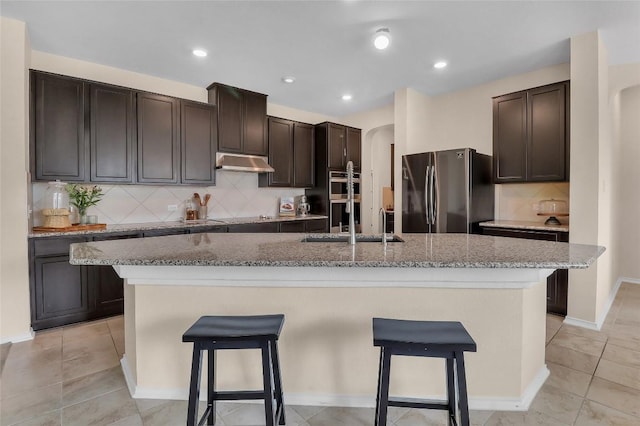 351 Jarbridge Dr, Kyle, TX 78640 - kitchen featuring appliances with stainless steel finishes, under cabinet range hood, arched walkways, a breakfast bar, and recessed lighting