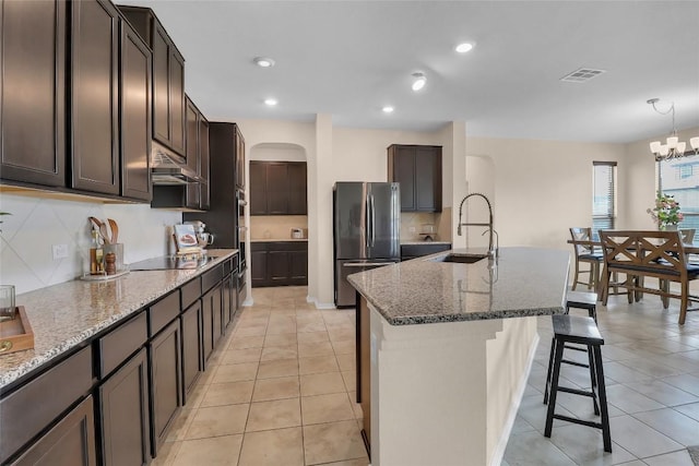 351 Jarbridge Dr, Kyle, TX 78640 - kitchen featuring freestanding refrigerator, arched walkways, under cabinet range hood, a kitchen breakfast bar, and dark stone counters