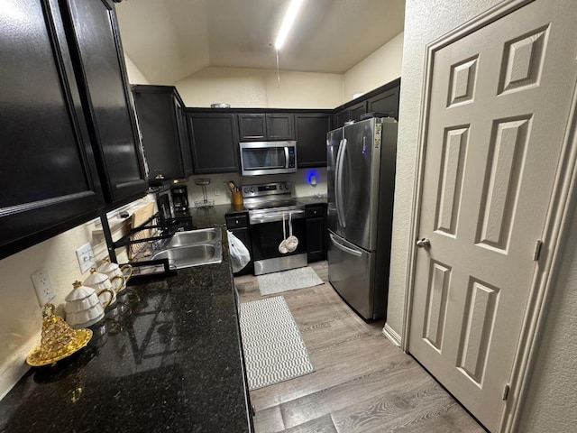 13409 Pine Needle St, Manor, TX 78653 - kitchen with stainless steel appliances, dark cabinets, lofted ceiling, light wood-style floors, and dark stone counters