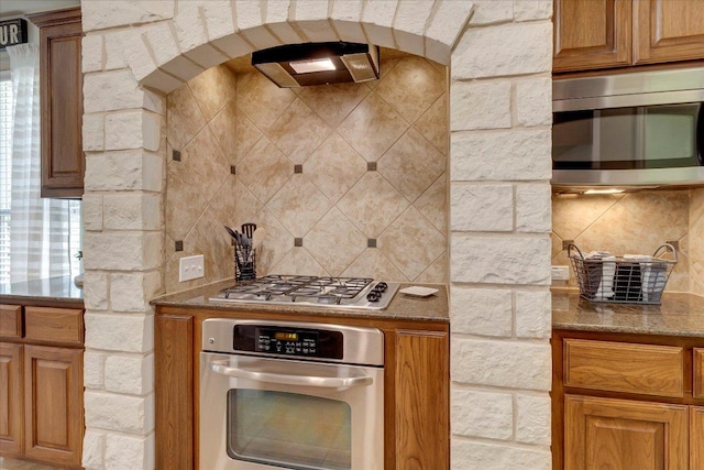 167 Limestone Trl Unit 76, Austin, TX 78737 - kitchen with appliances with stainless steel finishes, arched walkways, tasteful backsplash, and brown cabinets
