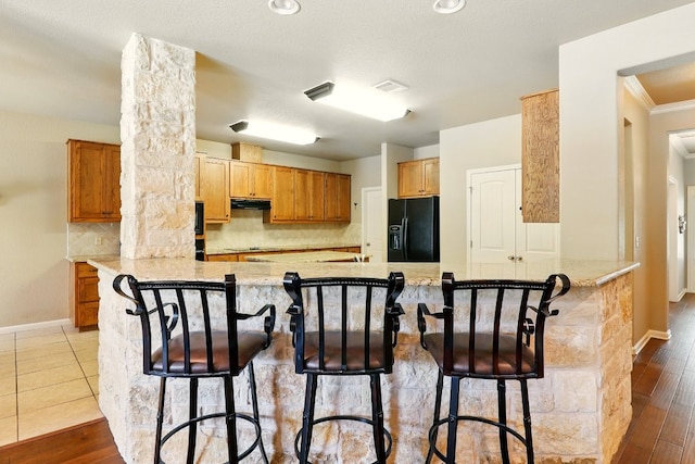 529 Honeycomb Cir, Driftwood, TX 78619 - kitchen with black fridge with ice dispenser, a peninsula, backsplash, under cabinet range hood, and a breakfast bar area