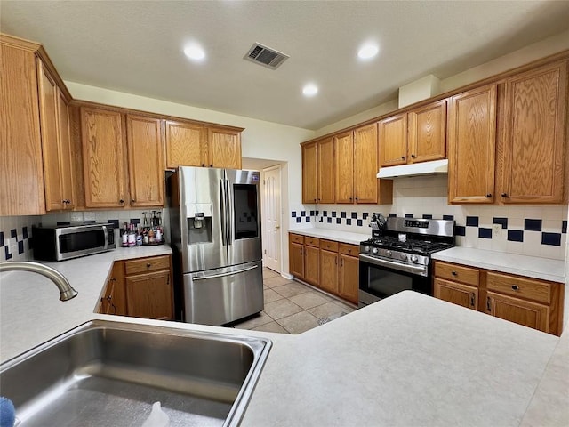 404 Autumn Trl, Georgetown, TX 78626 - kitchen with appliances with stainless steel finishes, a sink, tasteful backsplash, under cabinet range hood, and brown cabinetry