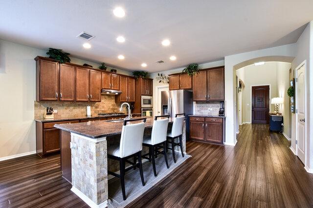 624 Purtis Creek Ln, Georgetown, TX 78628 - kitchen with appliances with stainless steel finishes, under cabinet range hood, arched walkways, an island with sink, and dark wood-style floors
