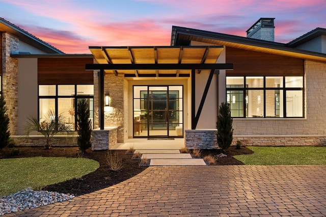 1047 Overlook Pkwy, Horseshoe Bay, TX 78657 - exterior entry at dusk with a chimney, stone siding, covered porch, and stucco siding