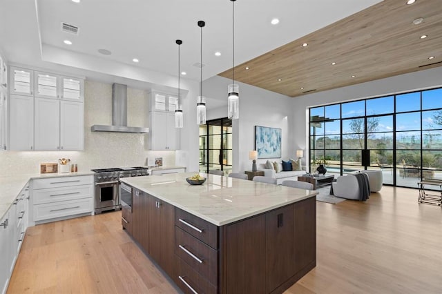 1047 Overlook Pkwy, Horseshoe Bay, TX 78657 - kitchen with wall chimney exhaust hood, light wood-style floors, dark brown cabinetry, a spacious island, and high end stove