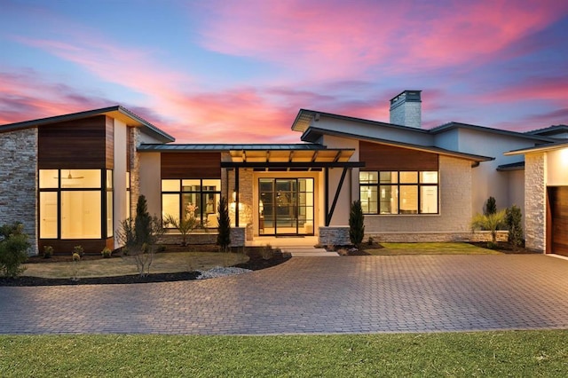 1047 Overlook Pkwy, Horseshoe Bay, TX 78657 - back of house at dusk with a chimney, a standing seam roof, a metal roof, driveway, and stone siding