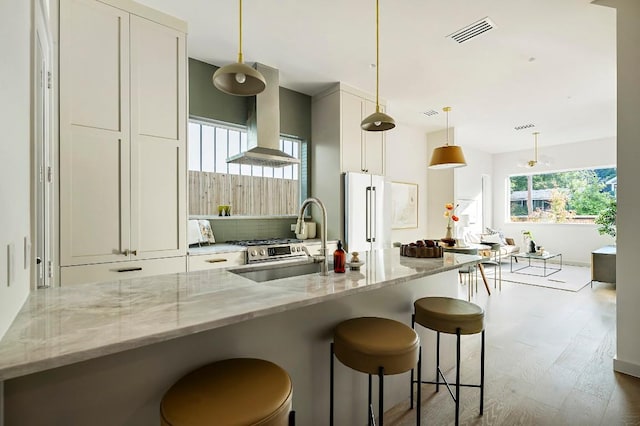 2109 Maple Ave, Austin, TX 78722 - kitchen featuring freestanding refrigerator, island exhaust hood, dark wood-style flooring, light stone countertops, and a kitchen bar