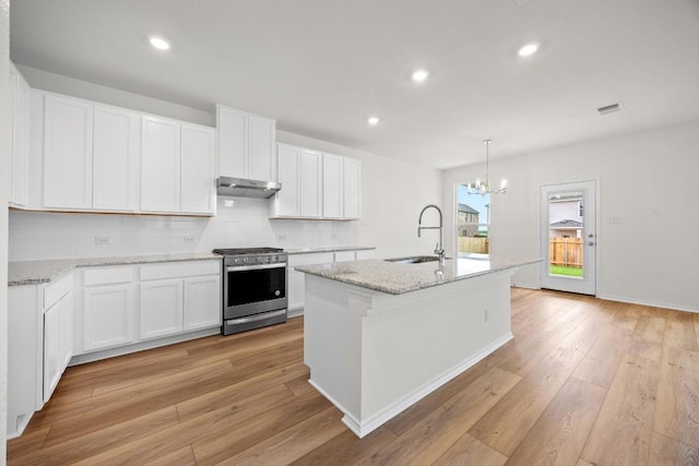 3917 Torraca Ln, Round Rock, TX 78665 - kitchen with stainless steel gas stove, under cabinet range hood, light wood-style flooring, backsplash, and a chandelier