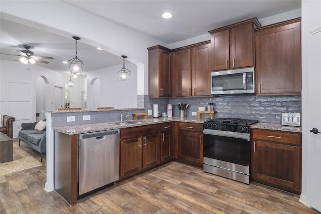 309 Callahan Ln, Leander, TX 78641 - kitchen with stainless steel appliances, arched walkways, a sink, dark wood finished floors, and a peninsula