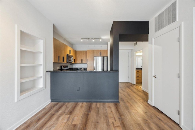 54 Rainey St Unit 815, Austin, TX 78701 - kitchen with stainless steel appliances, dark countertops, brown cabinets, a peninsula, and light wood finished floors