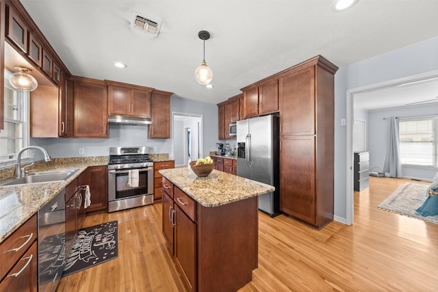 1902 N 7th St, Temple, TX 76501 - kitchen with stainless steel appliances, under cabinet range hood, a kitchen island, light wood-style floors, and light stone countertops