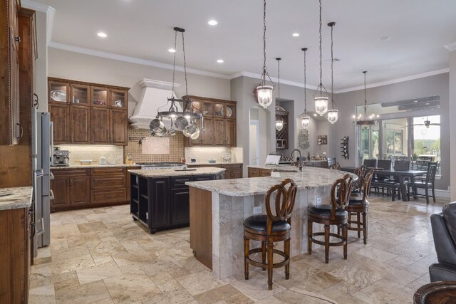 700 Zen Gardens Ter, Austin, TX 78732 - kitchen featuring a large island with sink, tasteful backsplash, custom range hood, stone tile floors, and a kitchen bar