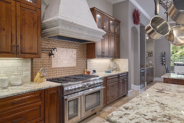 700 Zen Gardens Ter, Austin, TX 78732 - kitchen featuring custom exhaust hood, range with two ovens, ornamental molding, glass insert cabinets, and light stone counters
