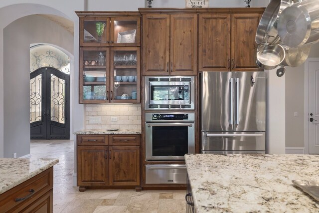 700 Zen Gardens Ter, Austin, TX 78732 - kitchen with stainless steel appliances, a warming drawer, arched walkways, decorative backsplash, and light stone counters