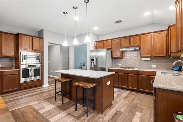 2313 Jake Pickle Pass, Leander, TX 78641 - kitchen with appliances with stainless steel finishes, light wood finished floors, brown cabinetry, a breakfast bar area, and tasteful backsplash