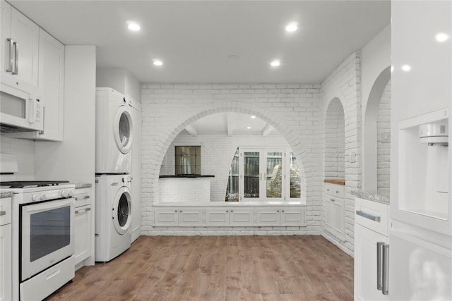 4202 N Hills Dr, Austin, TX 78731 - kitchen featuring white appliances, stacked washing machine and dryer, white cabinetry, light wood finished floors, and brick wall
