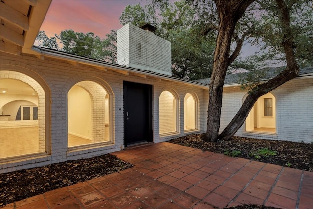 4202 N Hills Dr, Austin, TX 78731 - exterior entry at dusk featuring brick siding, a chimney, and a patio