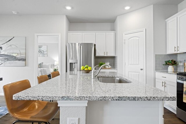 19825 Abigail Fillmore Rd, Manor, TX 78653 - kitchen featuring stainless steel refrigerator with ice dispenser, white cabinetry, an island with sink, decorative backsplash, and light stone countertops