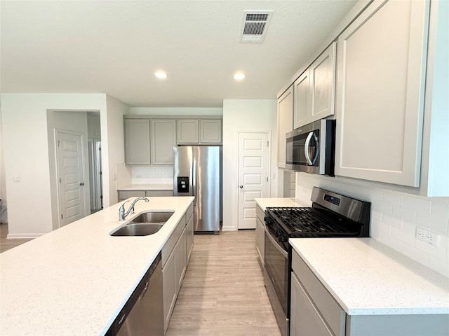 12006 Curlin Cv, Buda, TX 78610 - kitchen with stainless steel appliances, light wood finished floors, a sink, gray cabinets, and backsplash