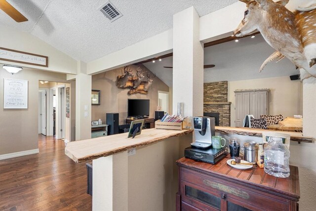 2201 Carolyn Dr, Taylor, TX 76574 - living area featuring a ceiling fan, lofted ceiling, dark wood-type flooring, a stone fireplace, and a textured ceiling