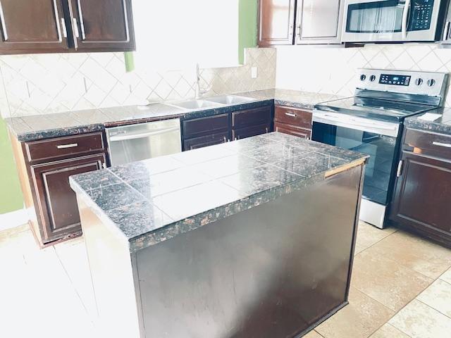 109 E Wheeler St S, Manor, TX 78653 - kitchen with appliances with stainless steel finishes, tile counters, backsplash, and dark brown cabinetry