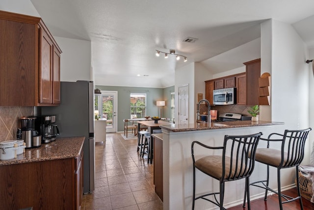 10304 Lone Pine Ln, Austin, TX 78747 - kitchen with stainless steel appliances, a peninsula, backsplash, dark stone countertops, and a breakfast bar area