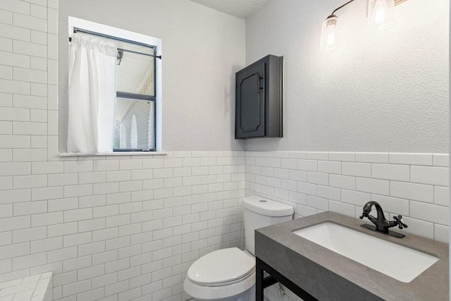 220 E Belton Ave, Rockdale, TX 76567 - bathroom with tile walls, toilet, vanity, and a wainscoted wall