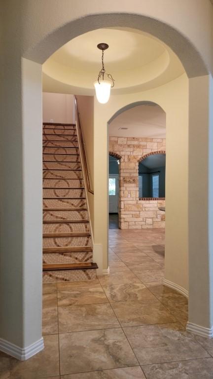 1002 Boxwood Loop, Georgetown, TX 78628 - hallway featuring stairs, baseboards, a tray ceiling, and arched walkways